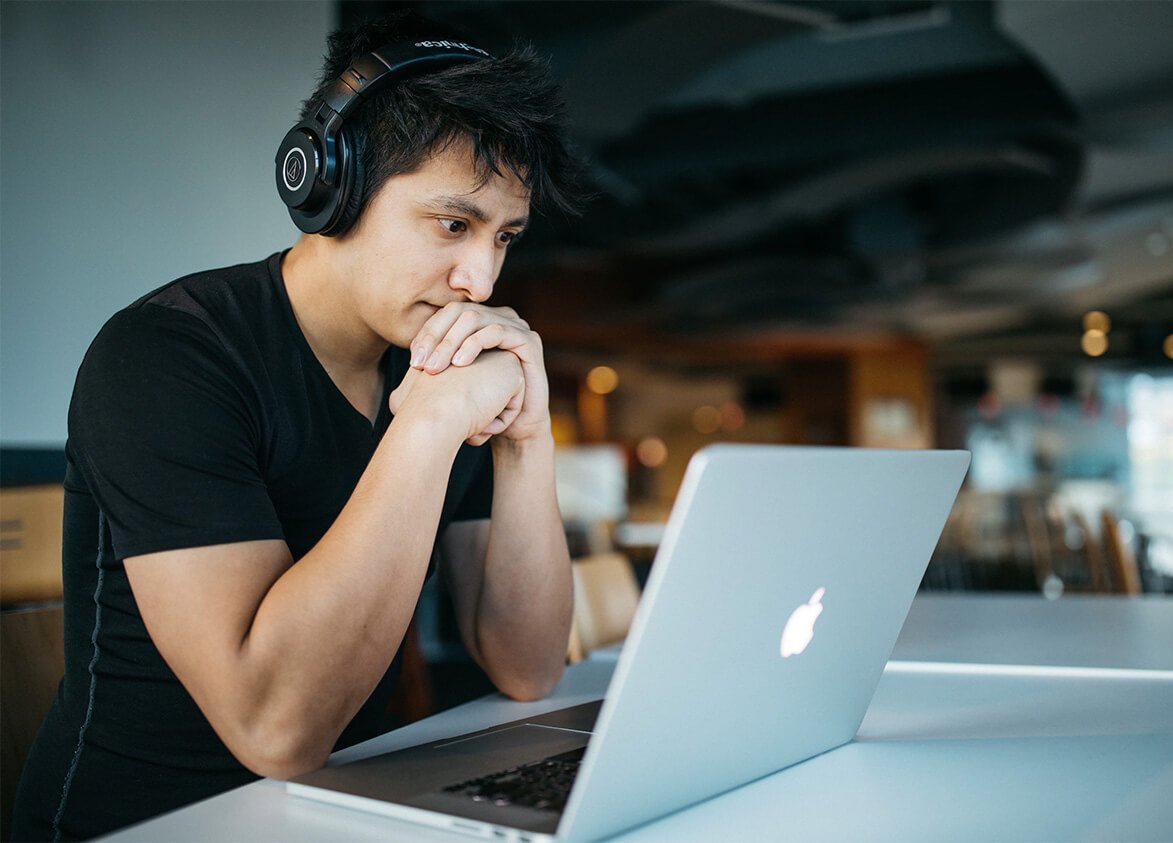 Eine Person sitzt mit Kopfhörern an einem Tisch und guckt konzentriert auf einen Laptop.