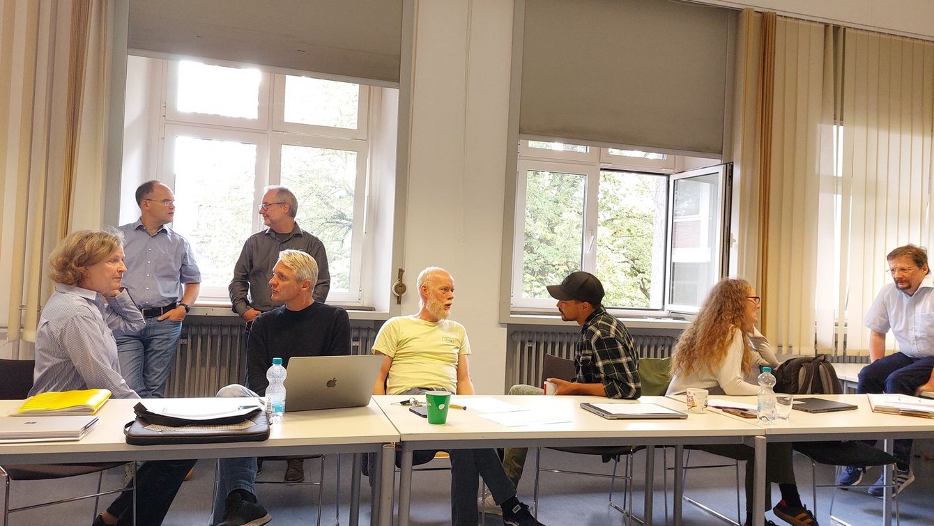 Ein Gruppenfoto von Personen, die in einem Hörsaal sitzen oder stehen und sich unterhalten.