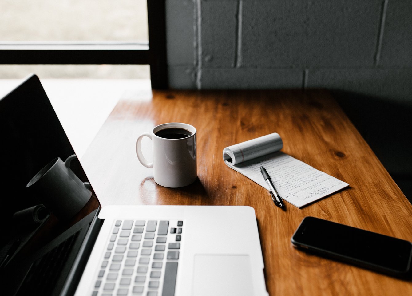 Schreibtisch mit Laptop, Tasse, Smartphone, Notizblock.